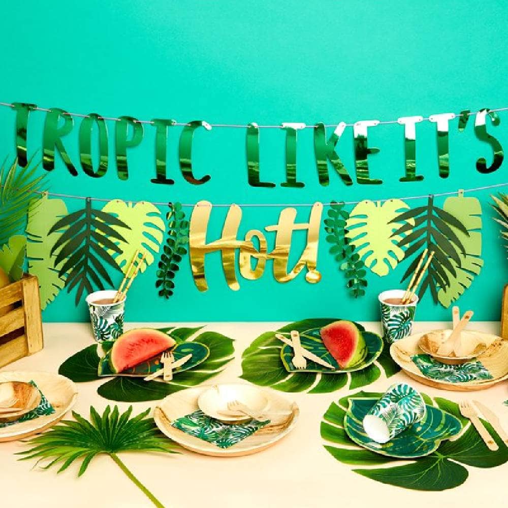 Tafel met tropische versiering zoals bordjes bekers en een slinger met tropische bladeren