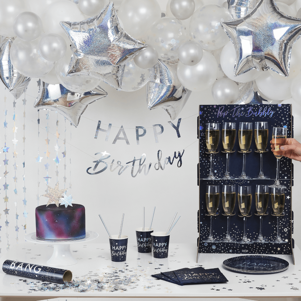 Ballonnen hangen boven een tafel met zilveren en zwarte verjaardagsversiering en een galaxytaart