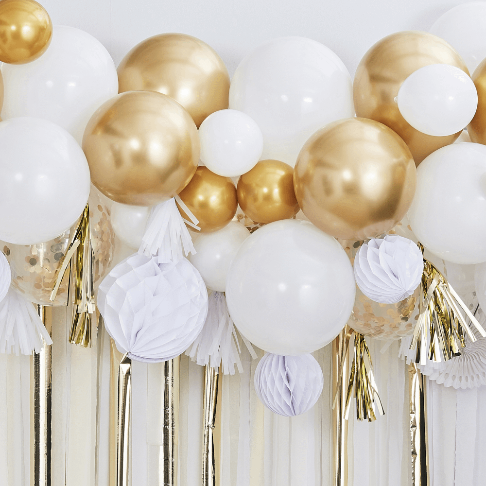 Witte en gouden ballonnen hangen voor een offwhite muur met wit en gouden glanzende streamers en witte honeycombs