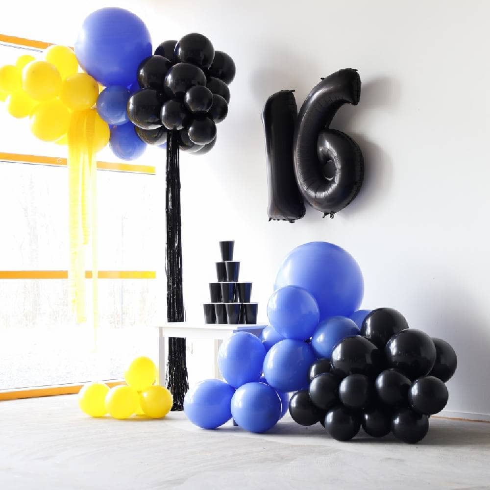 Zwarte cijferballonnen hangen aan een muur met daaronder blauwe, gele en zwarte ballonnen