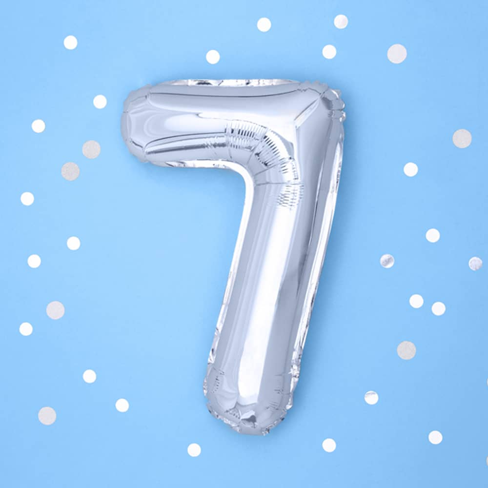 Zilveren folieballon cijfer 7 op een blauwe achtergrond met witte confetti