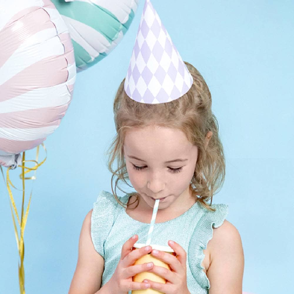 Kind met feesthoedje op en snoep folieballonnen drinkt uit rietje