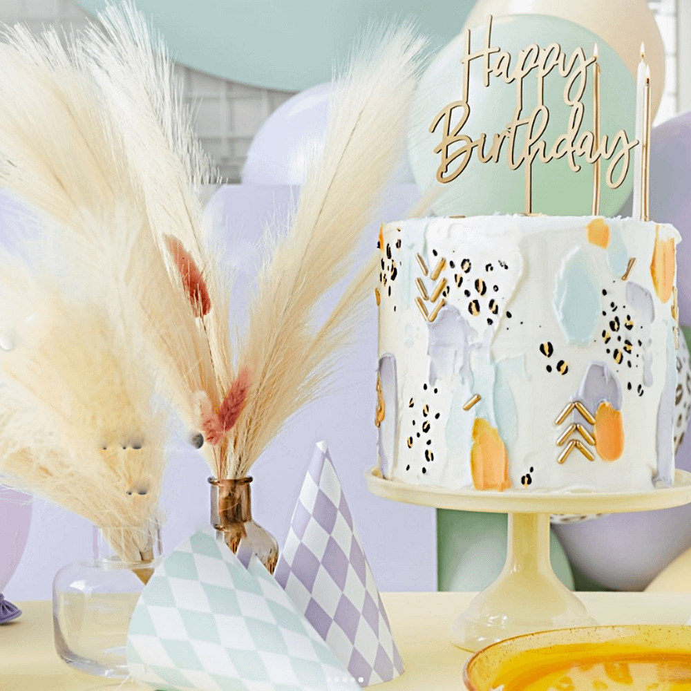 tafel versierd met pastel feesthoedjes, een taart met gouden kaartjes en beige veren