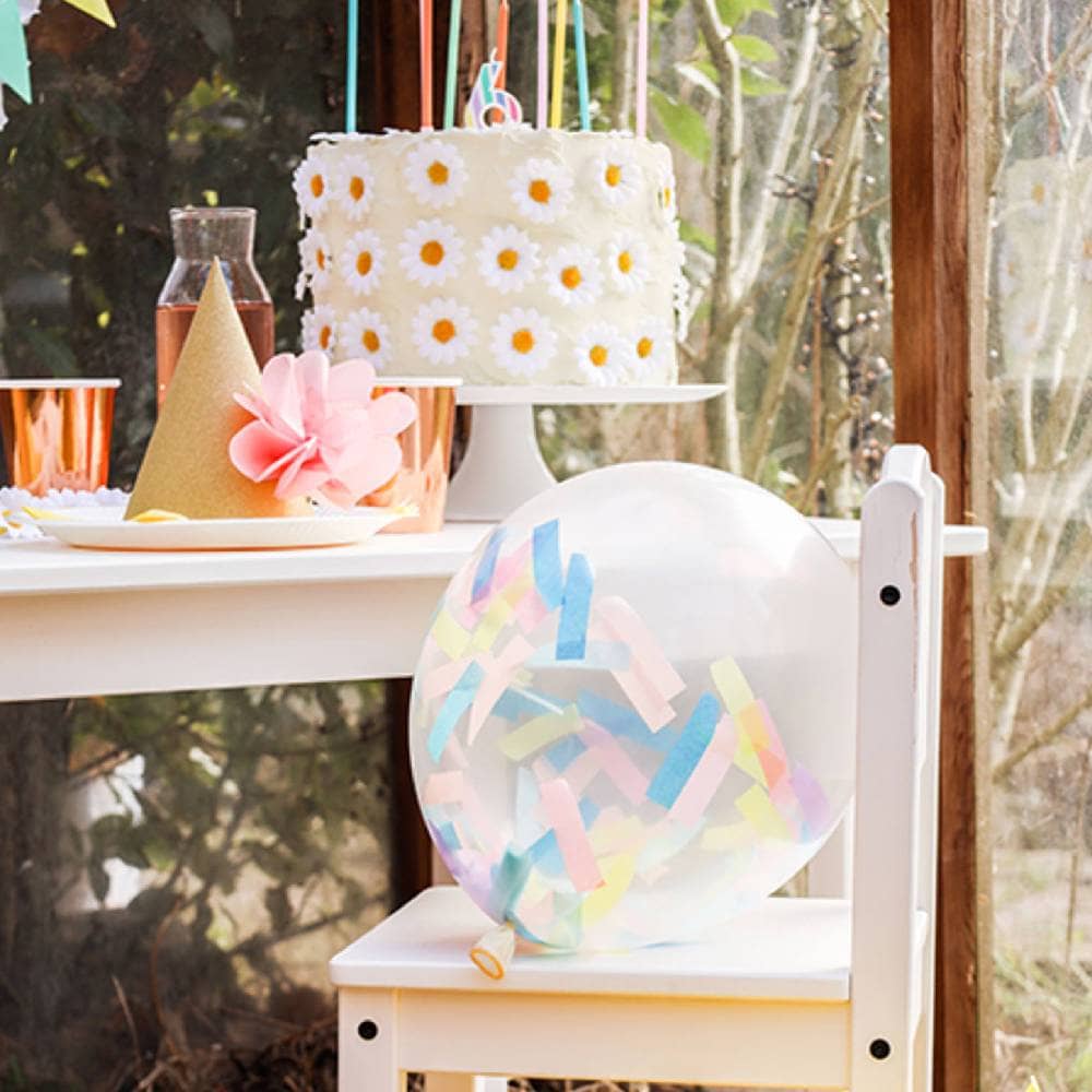 Tafel met bloemetjes taart met daarvoor een witte stoel met een confetti ballon erop