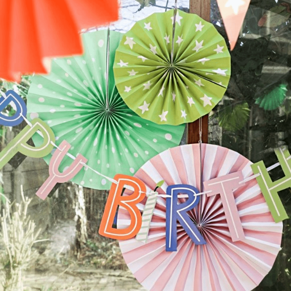 waaiers in het groen en roze met strepen, stippen en sterren hangen achter een slinger met de tekst happy birthday