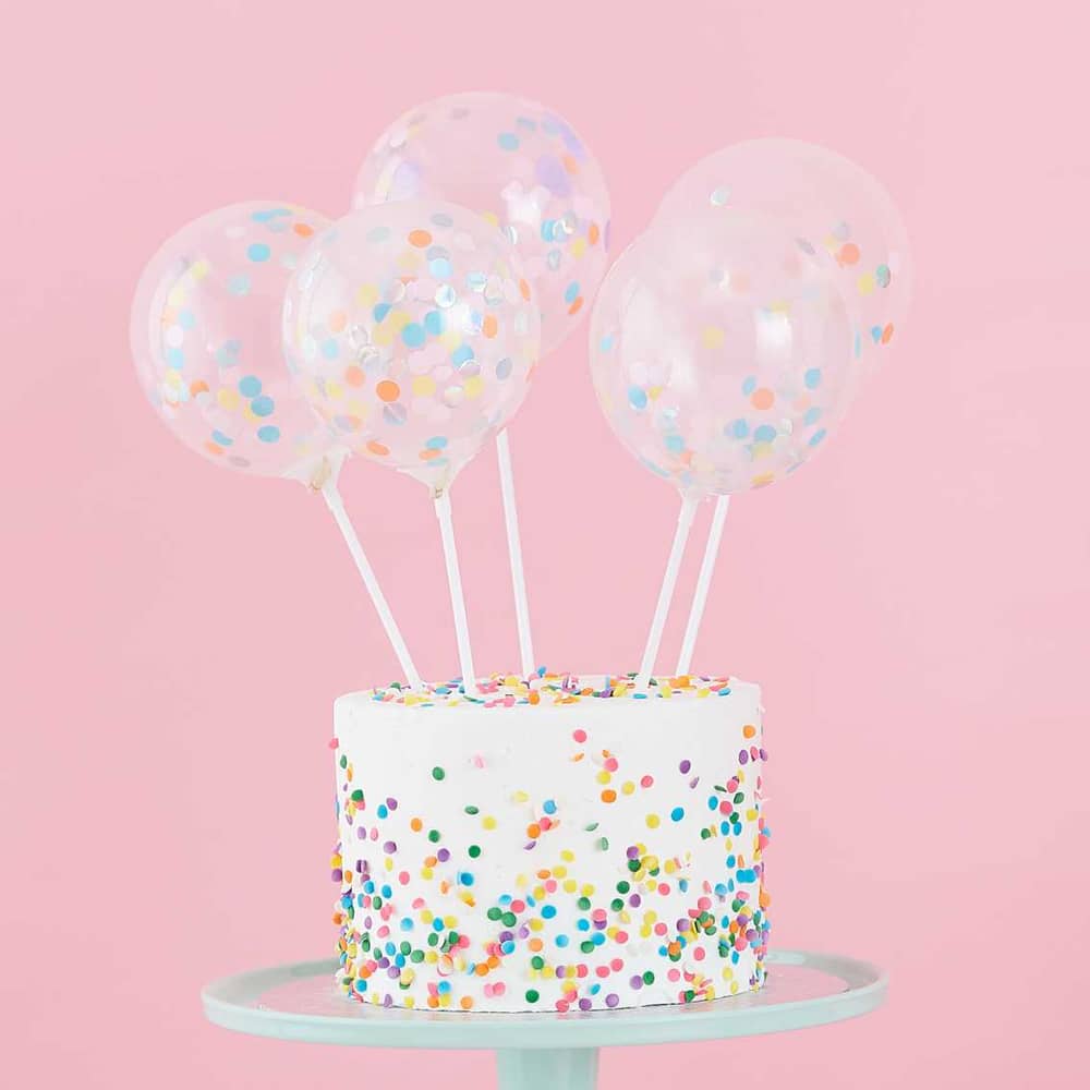 Vijf taart toppers met een ballon eraan in een taart met confetti erop