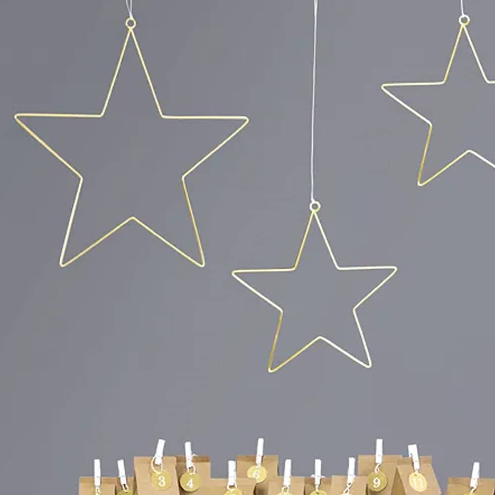 Metalen, gouden sterren hangen boven kaarsen bij grijze muur