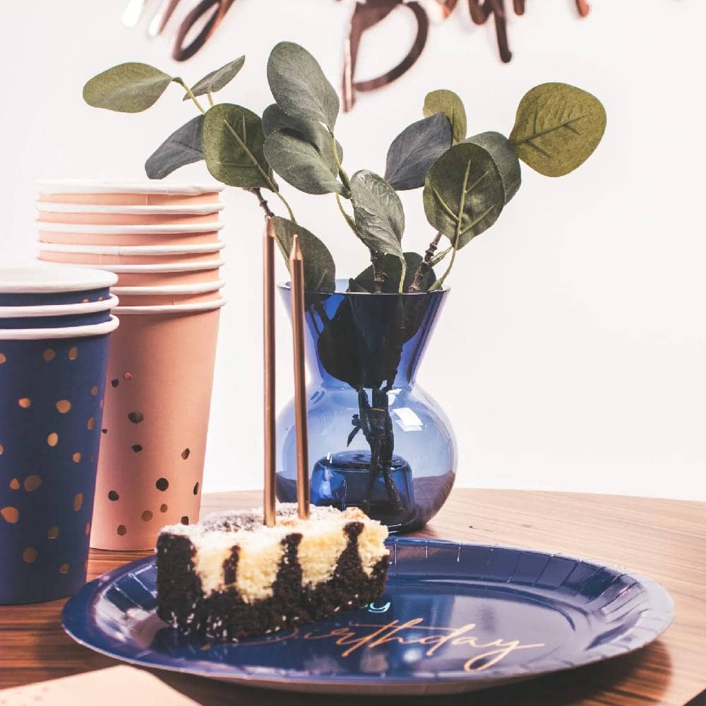 Blauw bordje met een stukje taart met daarachter blauwe en roze bekers en een blauw vaasje met plantjes erin