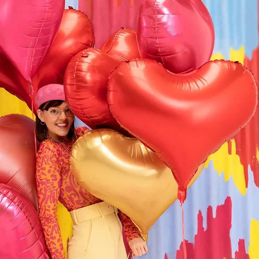 Vrouw met folieballonnen in de vorm van hartjes in de kleuren goud, rood, roze en rosé goud