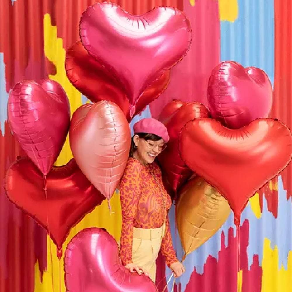Vrouw met een tros hartvormige ballonnen in de kleuren rood, roze, rosé goud en goud