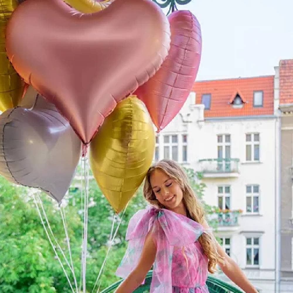 Vrouw in een roze jurk houd een set hartvormige ballonnen vast in de kleuren roze, lichtroze en goud