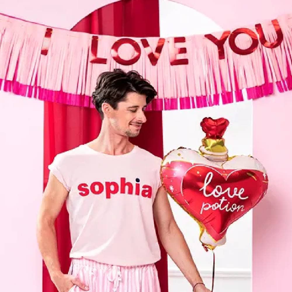 Man in roze pyjama met een folieballon in de vorm van een hart staat in een kamer met roze versiering