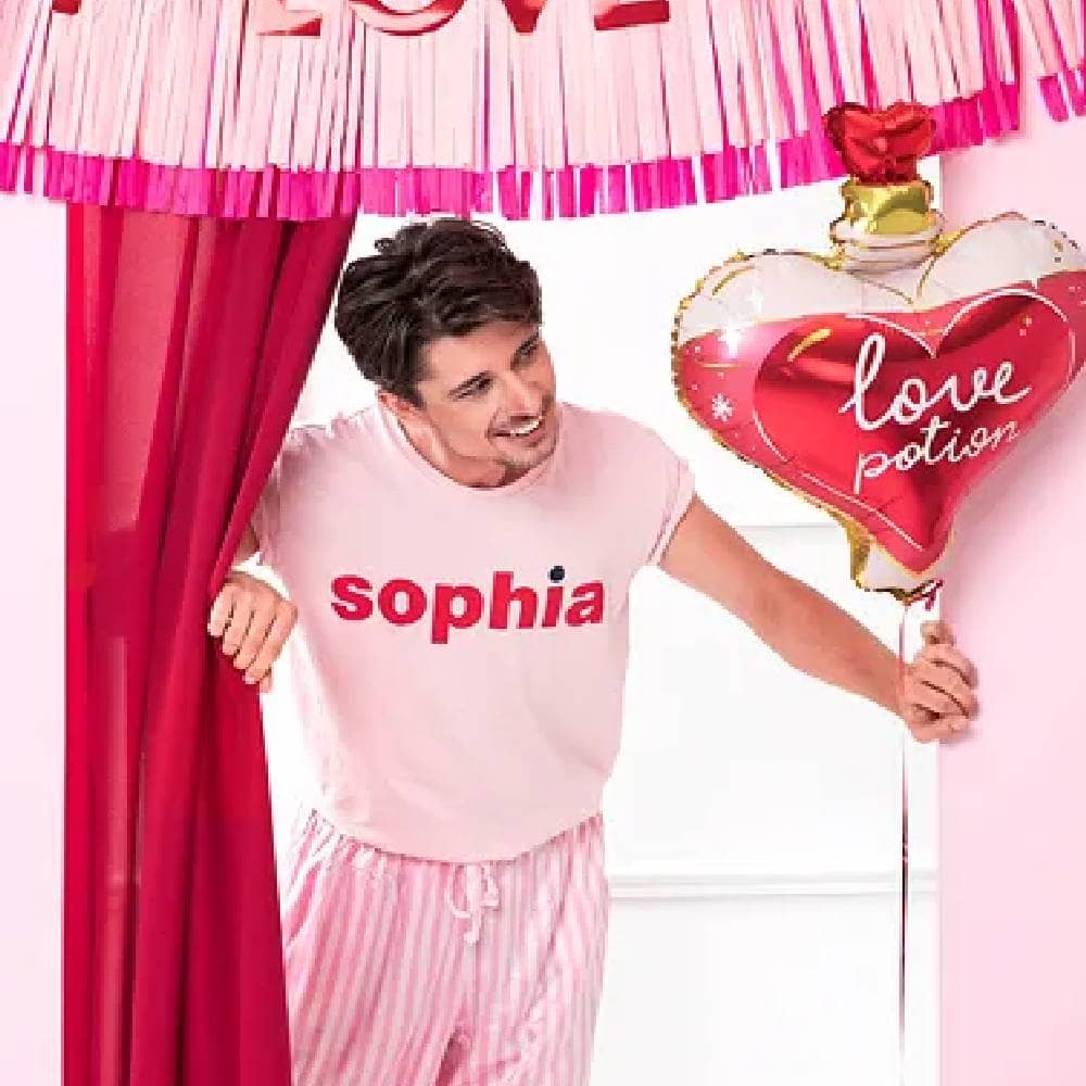 Man in roze pyjama met een folieballon in de vorm van een hart staat in een kamer met roze versiering