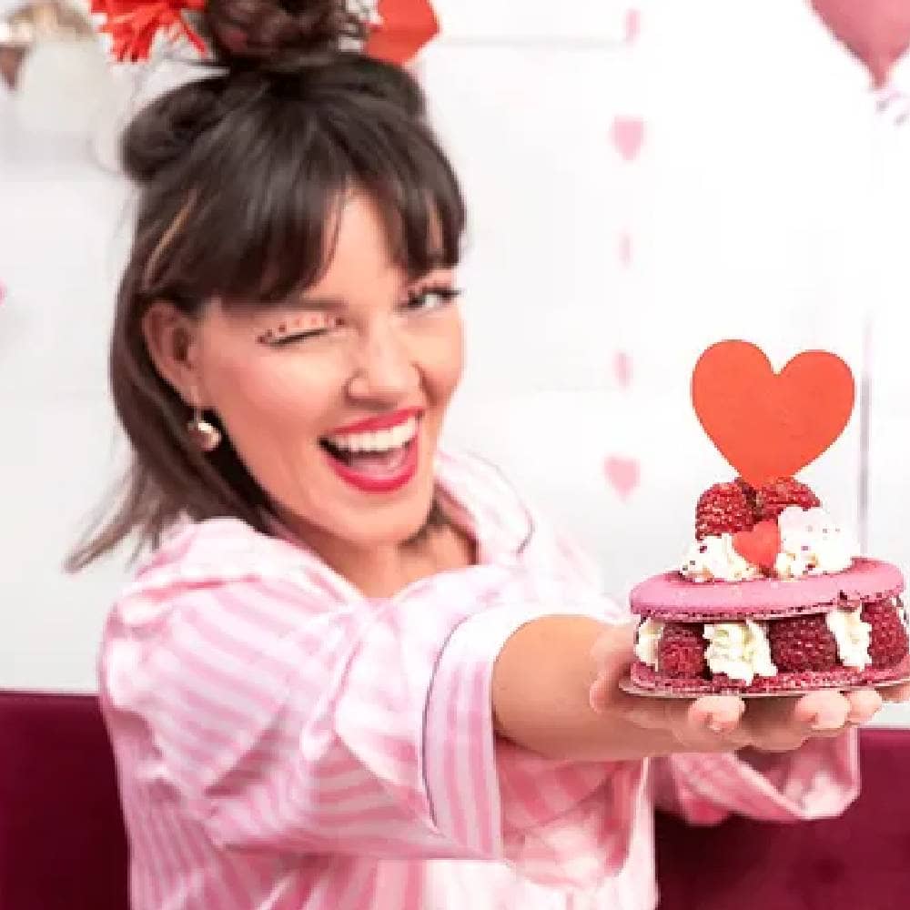 Vrouw met een roze macaron en een cupcaketopper met een rood hart