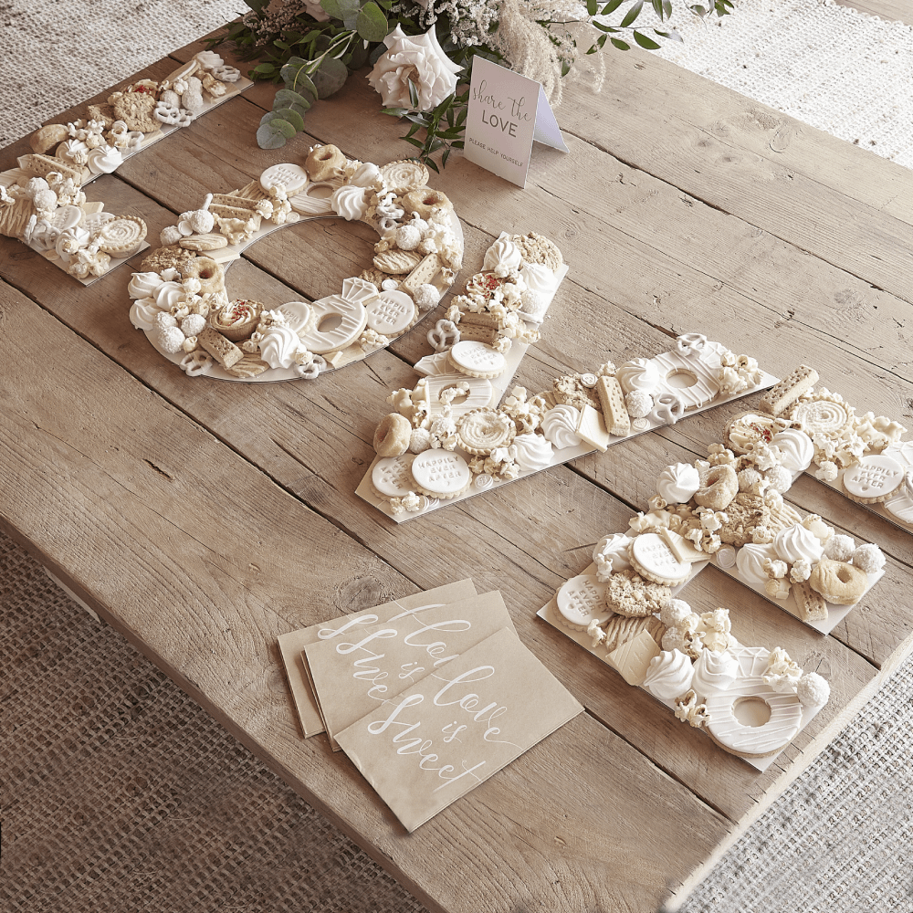 Houten tafel met witte letters LOVE gevuld met verschillende hapjes en een boeket met bloemen
