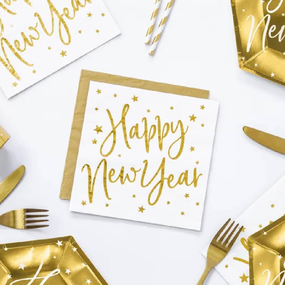 Witte servetten met gouden tekst 'happy new year' op een tafel met gouden bestek en papieren bordjes