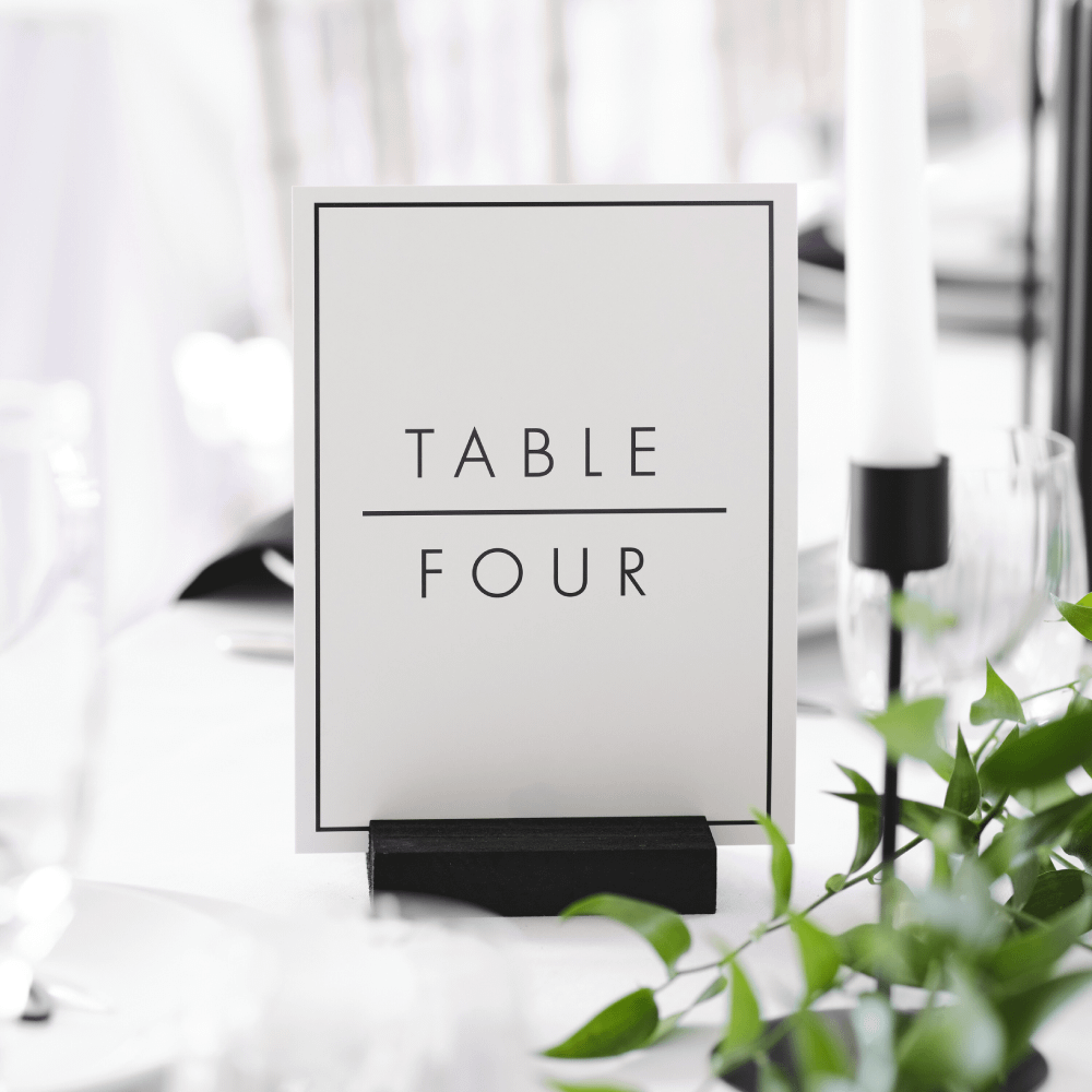Tafelnummer in het zwart en wit met strakke afwerking staat op een wit tafelkleed versierd met bladgroen