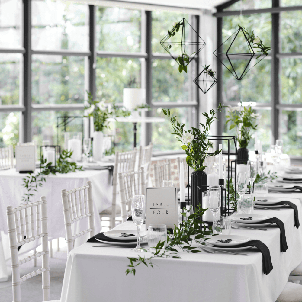 Witte feest tafel met zwarte versiering is versierd met planten en witte rozen
