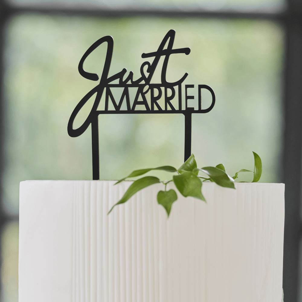 Zwarte taart topper met de tekst just married zit in een witte taart versied met een groen takje