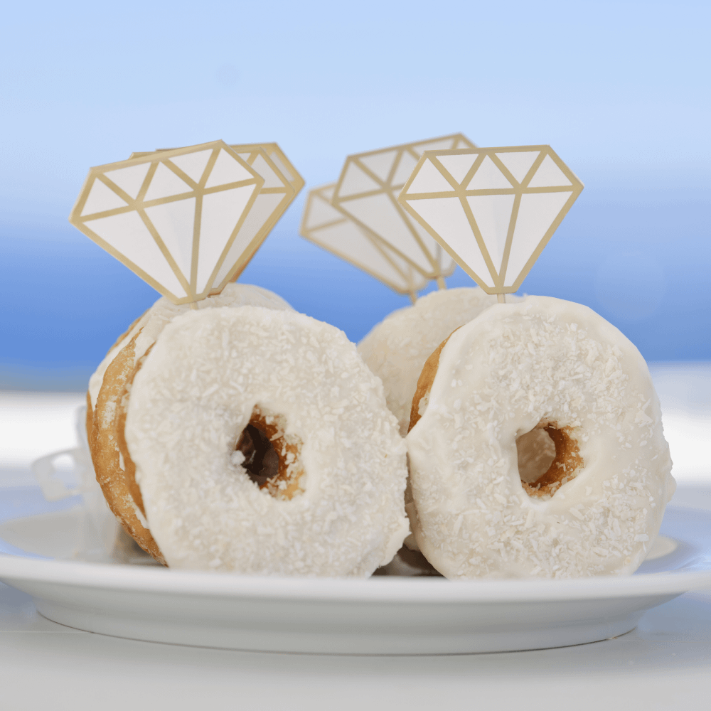 Witte donuts op een wit bord zijn versierd met toppers met gouden accentenen in de vorm van een diamant