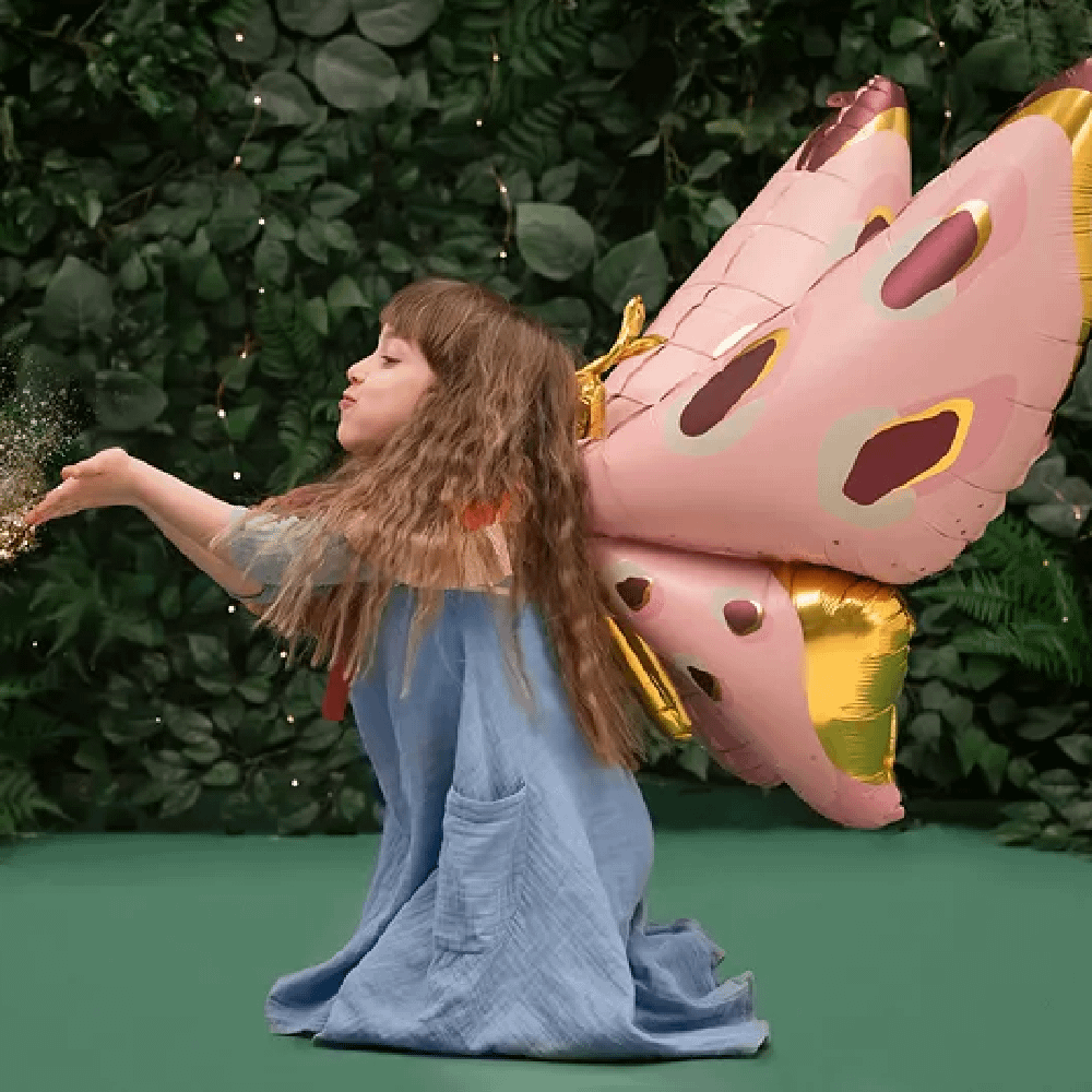 Meisje in een blauwe jurk heeft een folieballon in de vorm van een vlinder en blaast gouden confetti weg