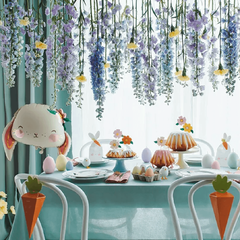 Tafel bedekt met lichtgroen tafelkleed en versierd met paaseieren, wortels en kuikentjes staat onder hangende lavendel