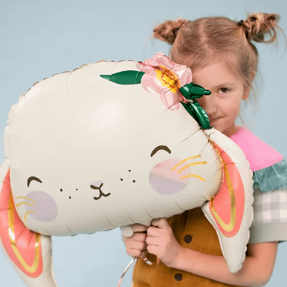 Meisje met twee knotjes houdt een folieballon vast in de vorm van een konijn met lichtoranje en gouden kleuren