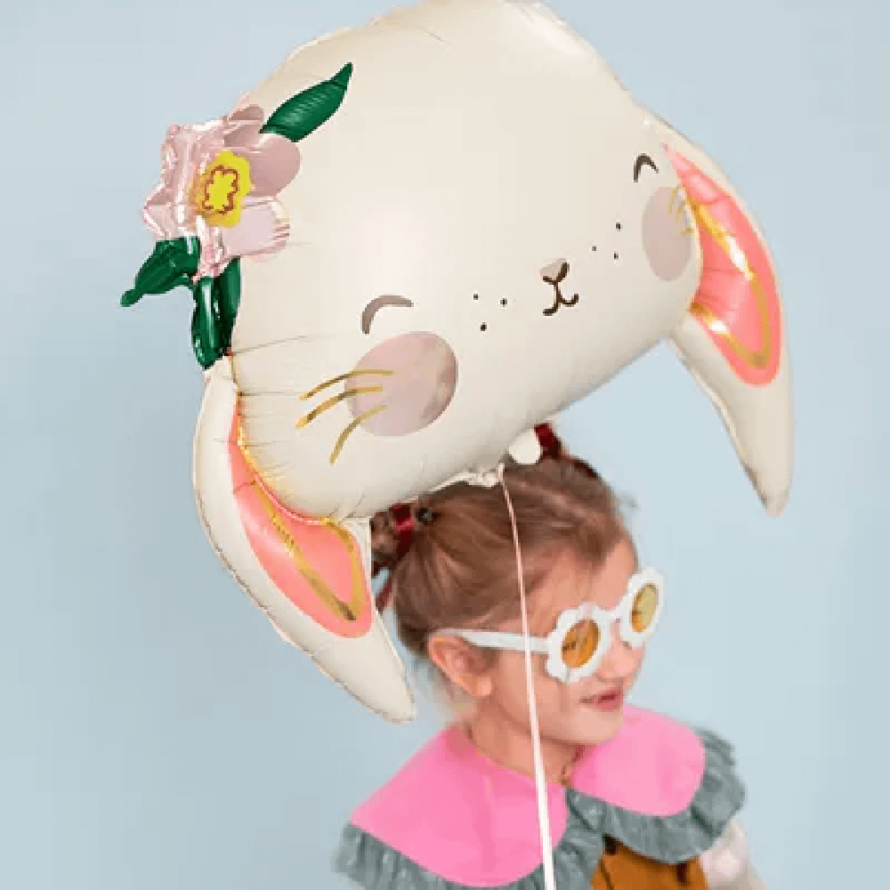Meisje met bruin haar en witte bril houd een folieballon vast in de vorm van een schattig konijntje