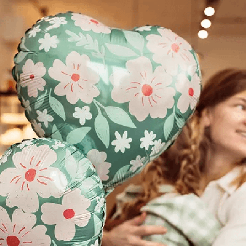 Vrouw houdt een groene ballon vast in de vorm van een hart met roze bloemenprint