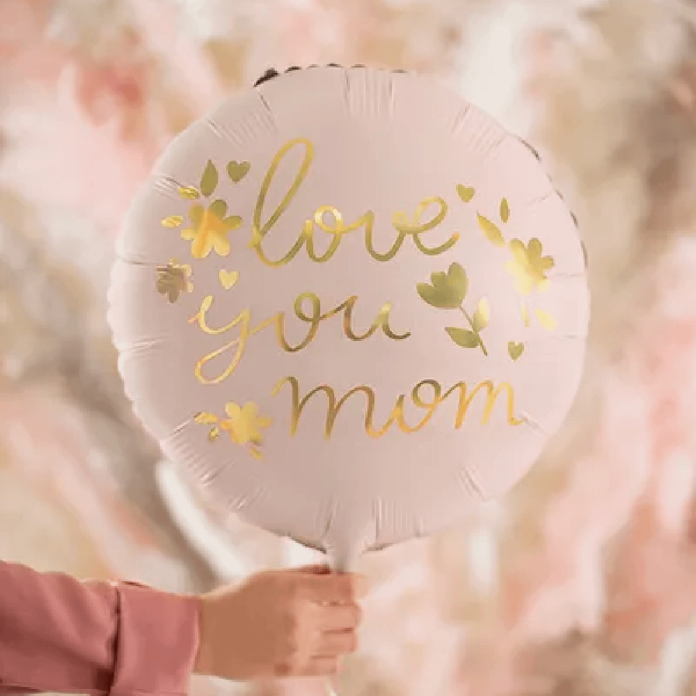 Lichtroze folieballon met gouden tekst 'love you mom' voor Moederdag wordt vastgehouden door een vrouw met een roze blouse