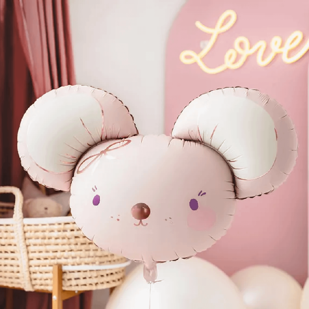 Folieballon van een lichtroze muisje met rose gouden details zweeft in een roze meisjeskamer met een rieten babymandje