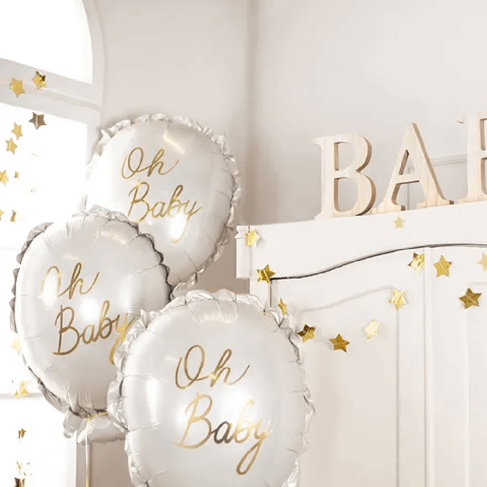 Drie folieballonnen in het wit met gouden tekst 'oh baby' zweven voor een houten, witte kast met houten letters 'baby'