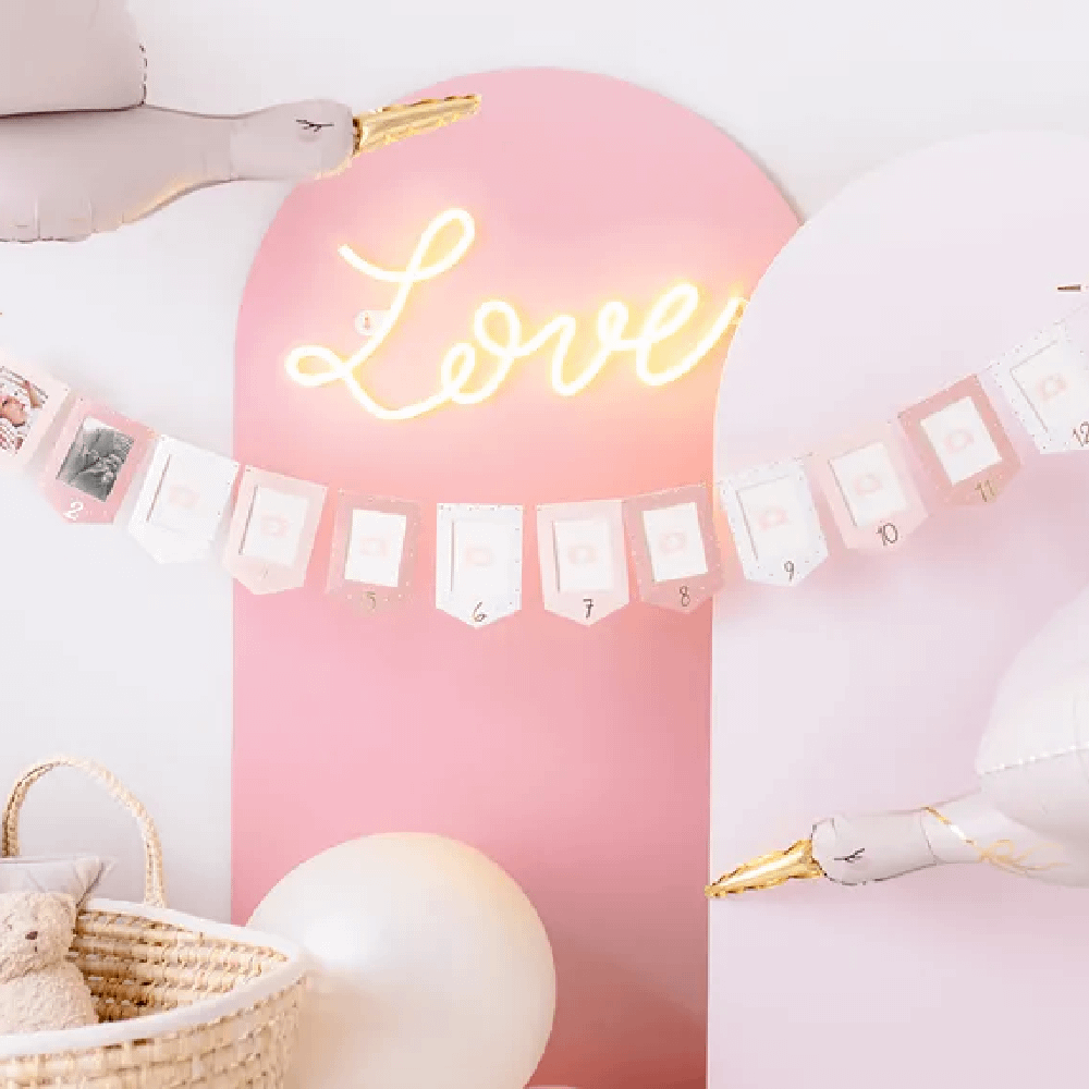 Roze kamer met ballonnen in de vorm van ooievaars, een fotoslinger en een ledlicht met de tekst 'love'