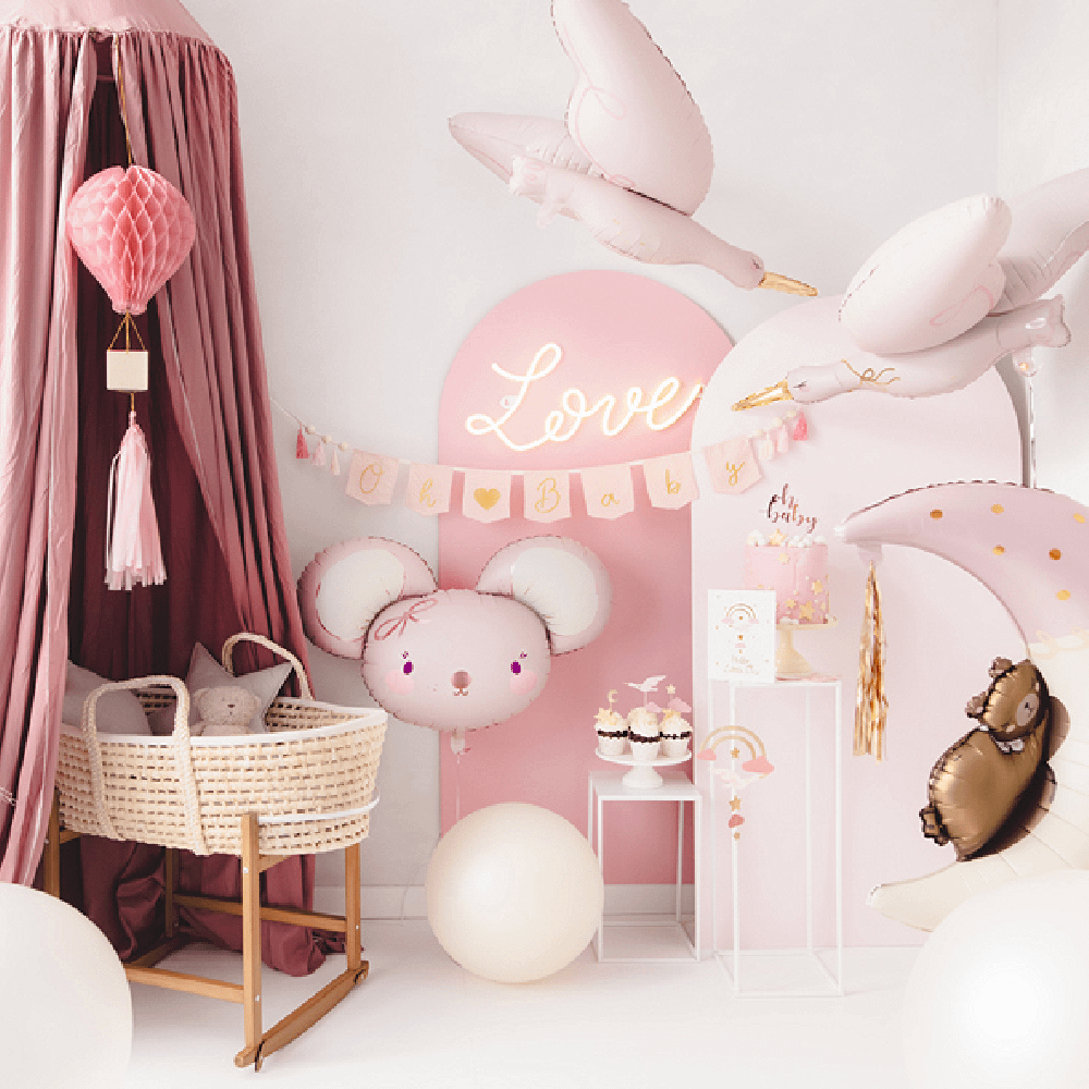 Roze babykamer met een rieten mandje, folieballonnen in de vorm van ooievaars en een roze honeycomb in de vorm van een luchtballon