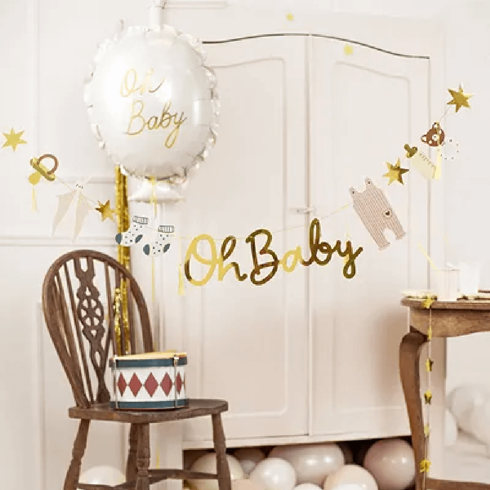 Slinger met de gouden tekst 'oh baby' hangt n een babykamer met beige en creme ballonnen en gouden sterretjes