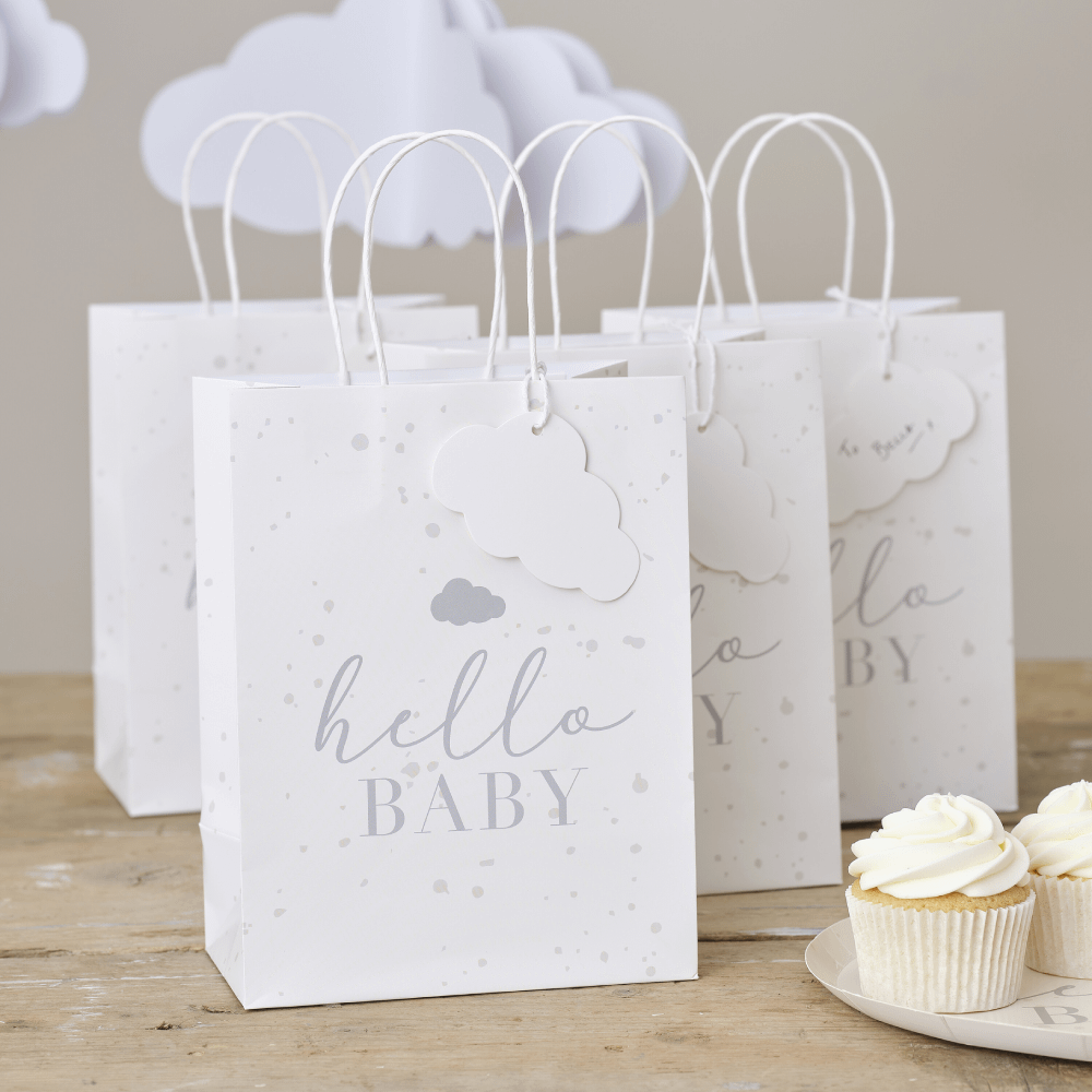 Witte giftbags voor een babyshower staan op een houten tafel naast cupcakes en erboven hangen witte wolkjes