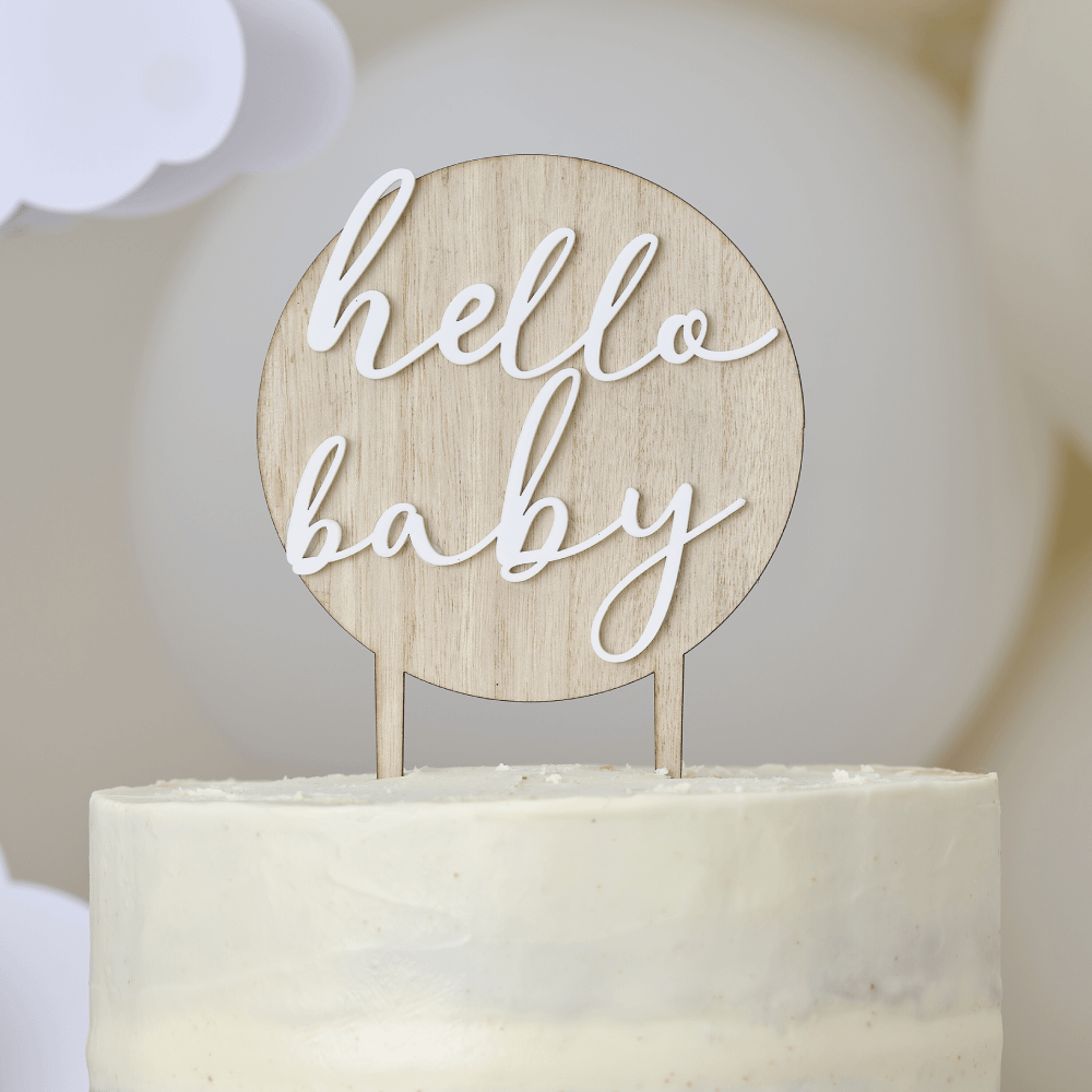 Ronde taarttopper gemaakt van hout met hierop de witte tekst 'hello baby' zit in een witte taart