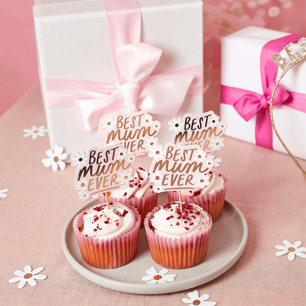 Cupcakes staan op een beige bord op een roze ondergrond en zijn versierd met prikkers met madeliefjes en de tekst best mum ever