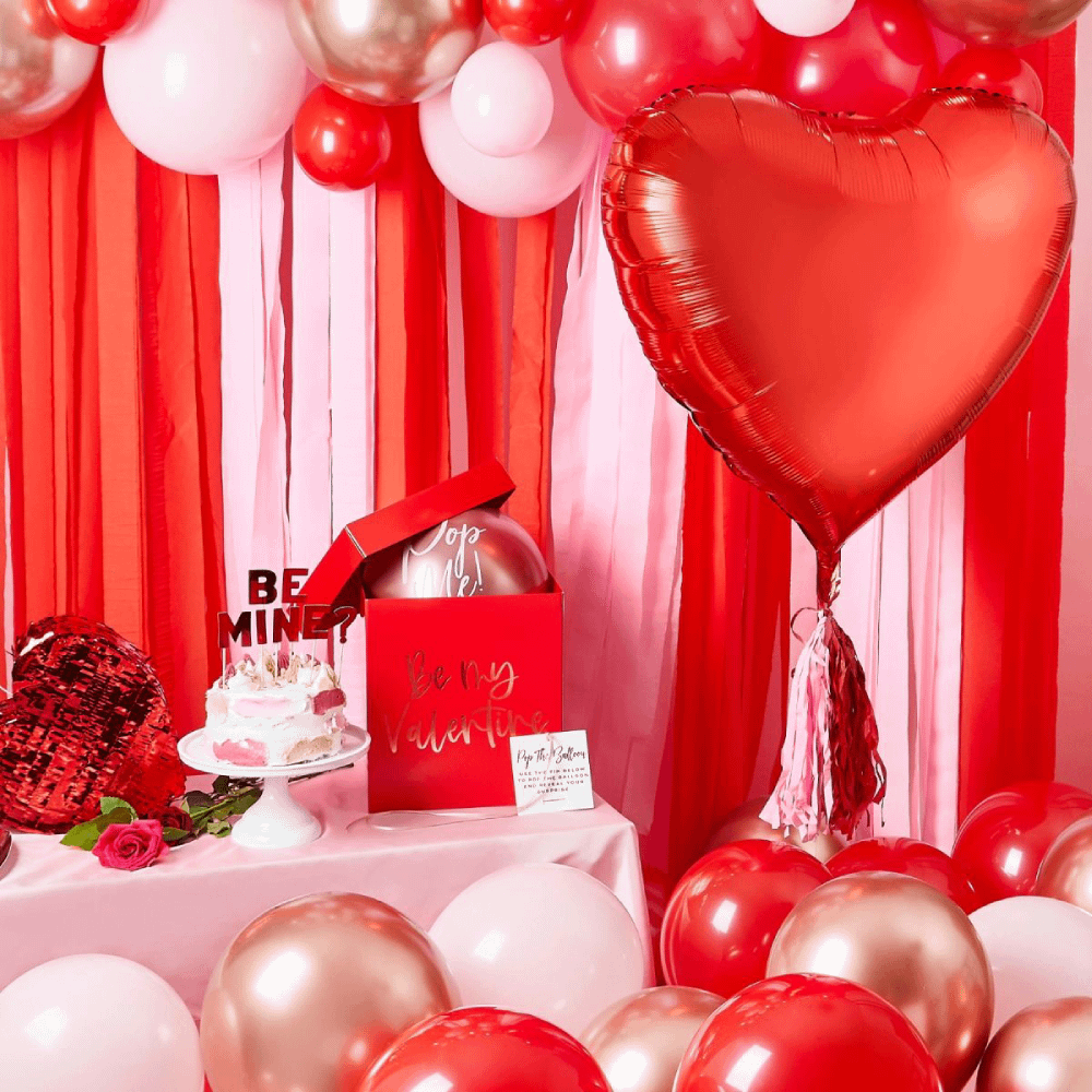 Rode en roze backdrop hangt achter een vloer gevuld met ballonnen en een versierde tafel