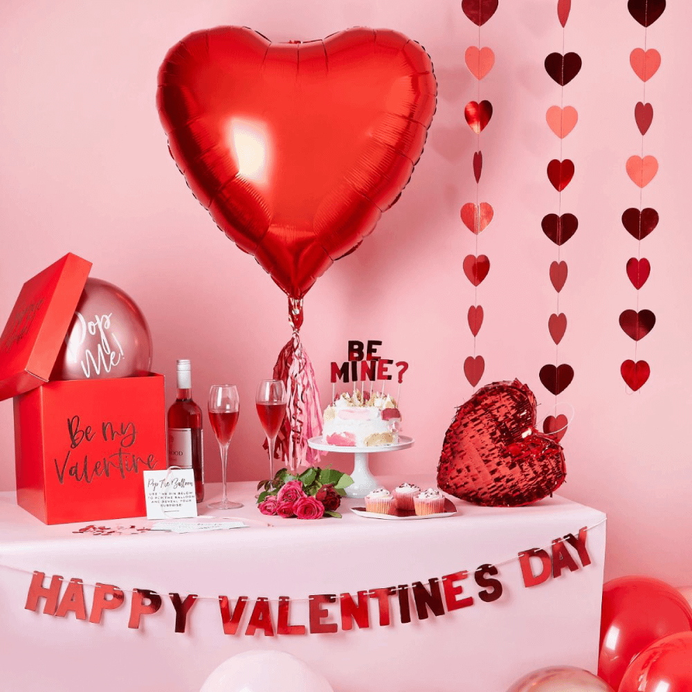 Roze tafel staat voor een roze muur en is versierd met rode Valentijnsversiering en twee glazen met rode champagne