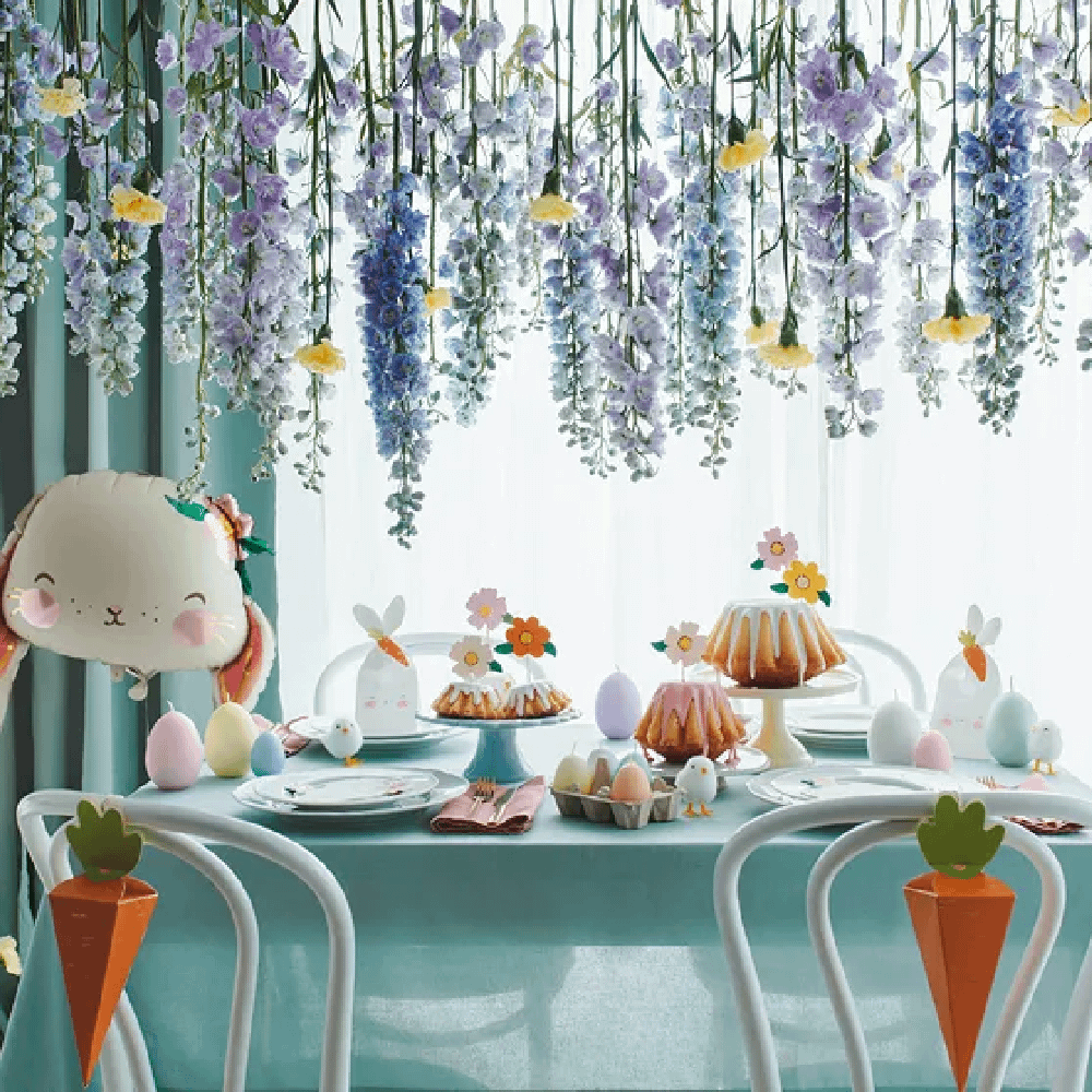 Tafel bedekt met lichtgroen tafelkleed en versierd met paaseieren, wortels en kuikentjes staat onder hangende lavendel