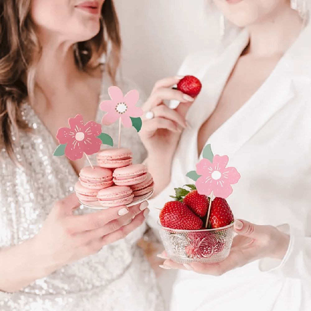 Twee vrouwen eten een bakje aardbeien en een schaaltje macarons versierd met cupcaketoppers met roze bloemen
