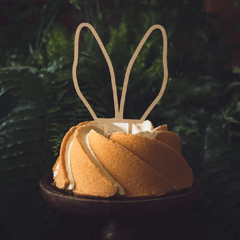 Houten taart topper in de vorm van konijnenoren in een cake krans op een houten plateau