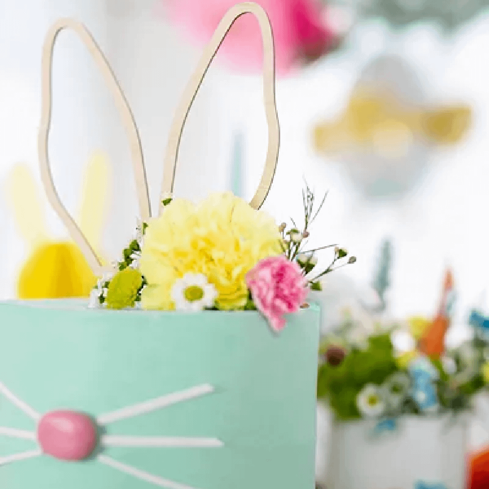Blauwe taart met konijnenoren en een roze neusje is versierd met gekleurde bloemen
