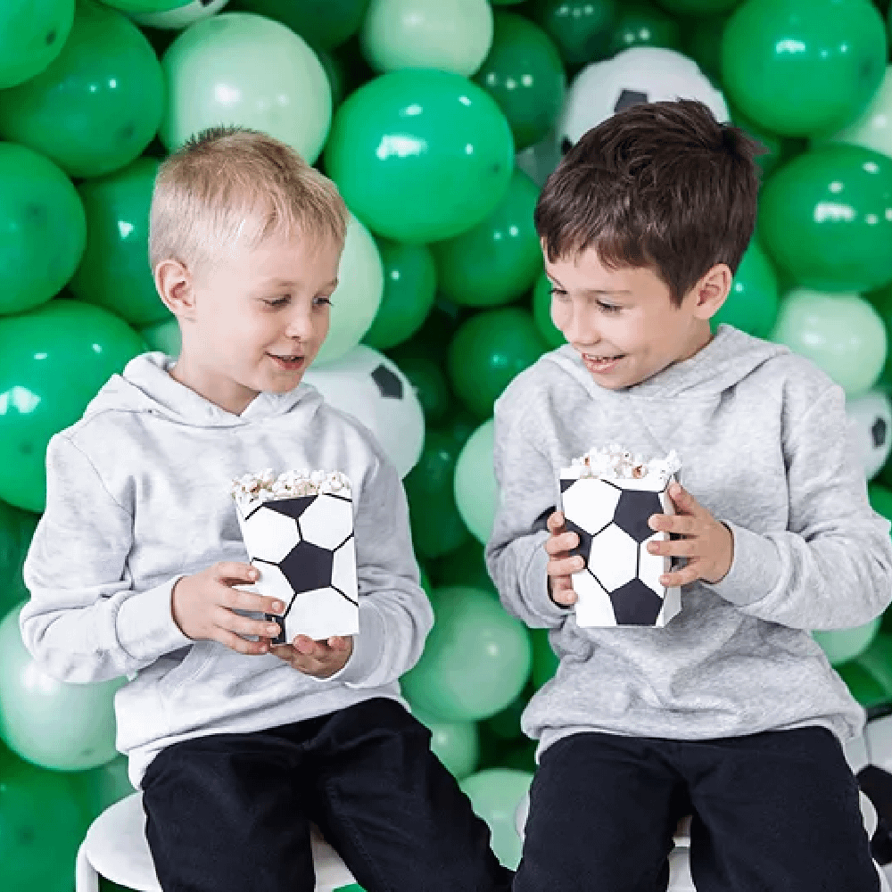 Twee jongens zitten voor een muur van groene ballonnen met een bakje bedrukt met een voetbal