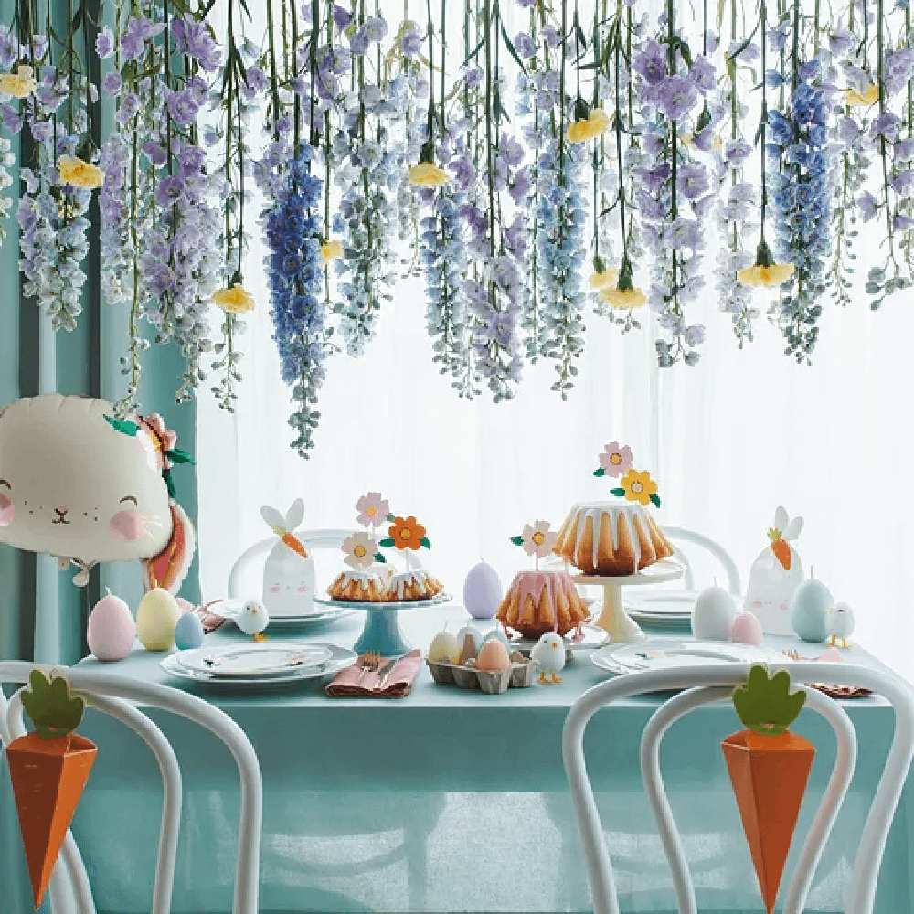 Feesttafel versierd met een ballon in de vorm van een konijn, bloemen die van het plafond afhangen en pastelkleurige paaseieren