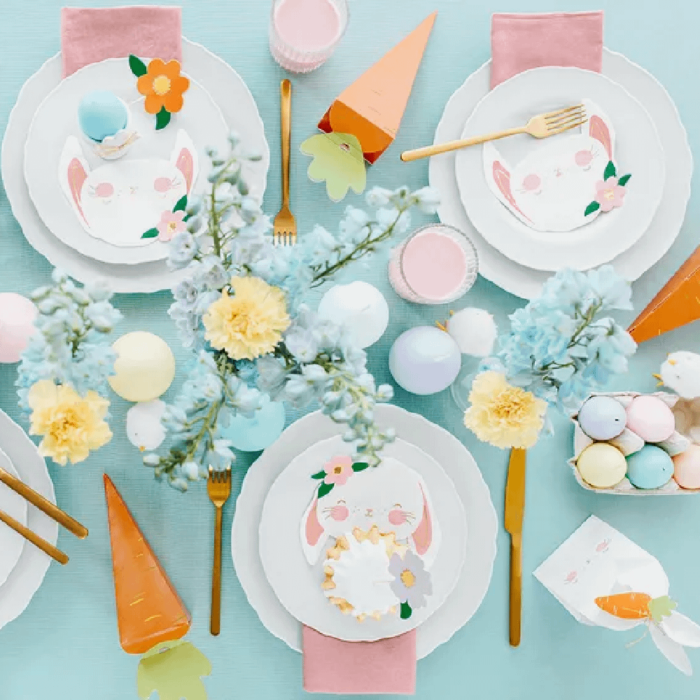Lichtblauwe tafel versierd met wortels, roze servetten en pastelkleurige paaseieren