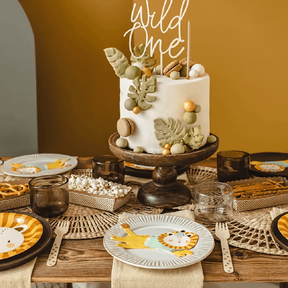 Houten tafel versierd met een donkerbruin plateau met een witte taart ,versierd met groene bladeren en rieten onderzetters