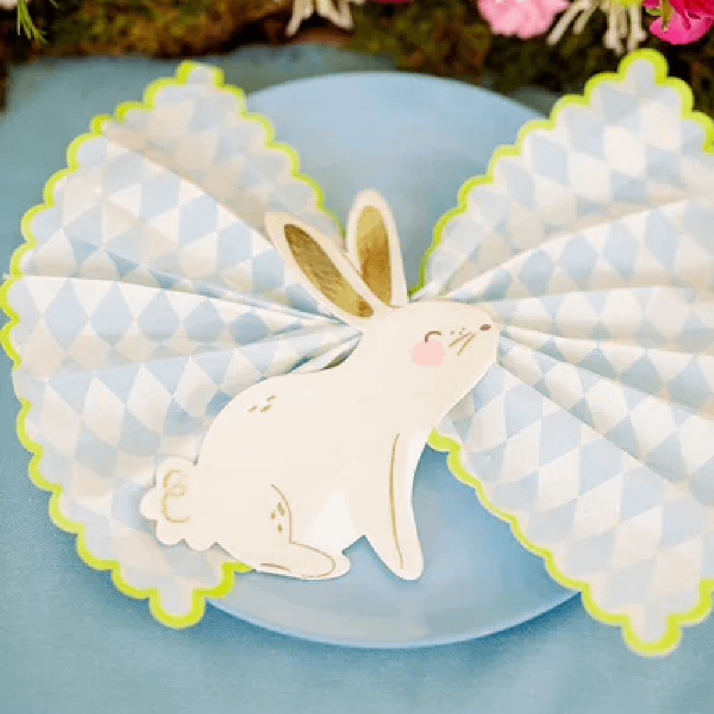 Servet in de vorm van een konijntje met gouden details ligt op een blauw bord