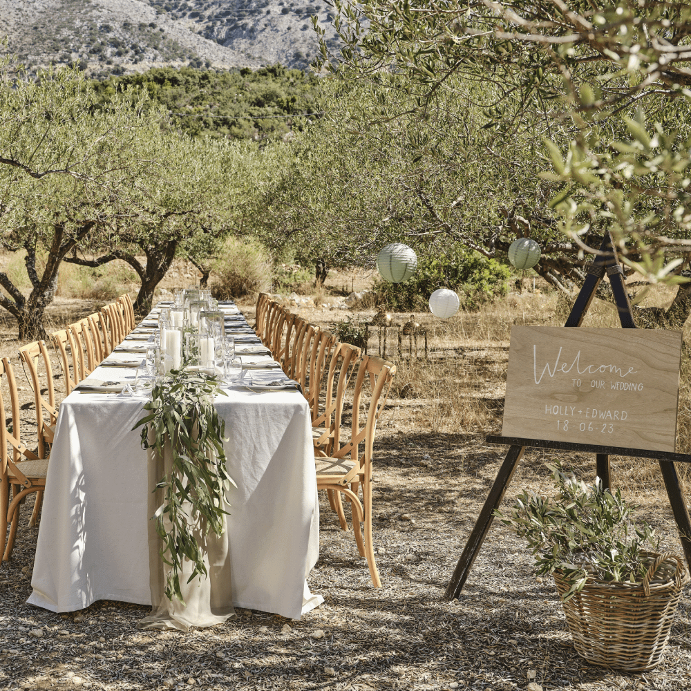 Tafel met wit tafelkleed en sage tafelloper staat in een veld met houten stoelen
